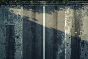 Aerial shot of a road with double white lines, flanked by textured concrete and greenery.