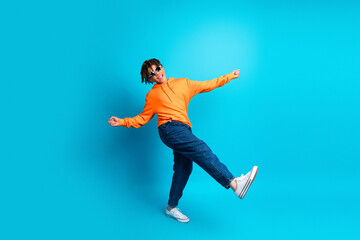 Fototapeta premium Teen boy in orange hoodie poses playfully against a blue background, showing trendy style and youthful energy