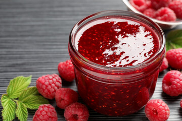 Sweet raspberry jam in glass jar and berries on dark gray wooden table, closeup
