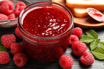 Sweet raspberry jam in glass jar and berries on dark gray table, closeup