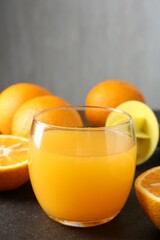 Fresh orange juice in glass, fruits and juicer on black table, closeup