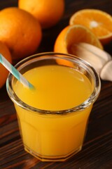 Fresh orange juice in glass, fruits and juicer on wooden table, closeup