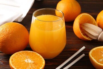 Fresh orange juice in glass, fruits, straws and juicer on wooden table, closeup