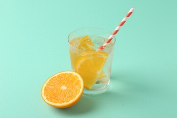 Sparkling water with orange slices in glass and fresh fruit on turquoise background, closeup