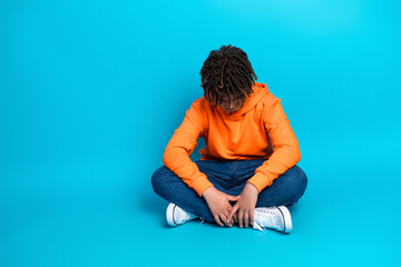 Young boy in casual orange hoodie seated on blue background showcasing stylish fashion and youthful energy