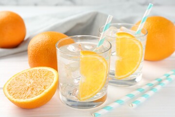 Sparkling water with orange slices in glasses and fresh fruits on white wooden table, closeup