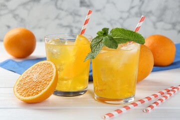 Refreshing soda water with orange slices in glasses, mint and fresh fruits on white wooden table, closeup