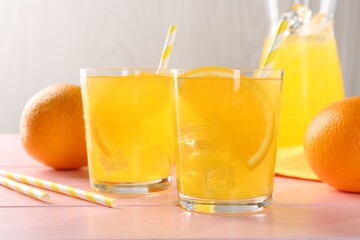 Refreshing soda water with orange slices in glasses, jug and fresh fruits on pink wooden table, closeup