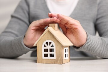 Home security. Woman protecting house model at white table, closeup