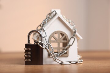 Home security. House model with chain and padlock on wooden table indoors