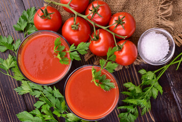 Tomato juice in glasses and tomatoes on a branch on a dark wooden background. Flat lay.
