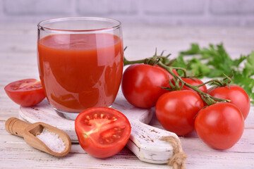 Tomato juice in a glass and tomatoes on a branch on a white wooden background.
