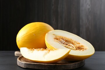 Cut and whole ripe melons on black wooden table, closeup