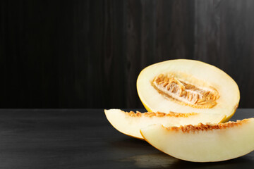 Cut ripe melon on black wooden table, closeup. Space for text