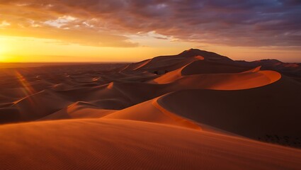 Obraz premium Golden desert dunes at sunset with dramatic clouds and distant mountains