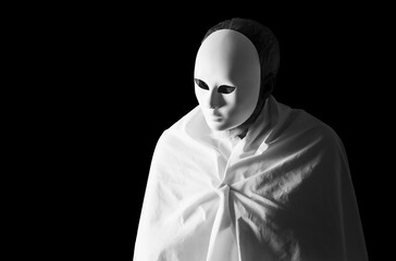 Human figure with white mask wrapped in a white drape on a black background.