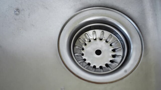 Water drain down on stainless steel kitchen sink hole, cleaning and hygiene concept.