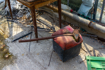 Old abandoned greenhouse with a rusty axe lying on a red pouffe, next to a metal table, rubble and...