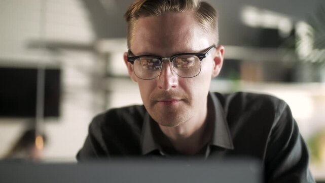 Professional Creative Man Sitting At His Desk In Home Office Studio Working Typing On a Laptop. Young Male Professional Using Computer Sitting At Office Desk. Busy Worker Freelancer Working On