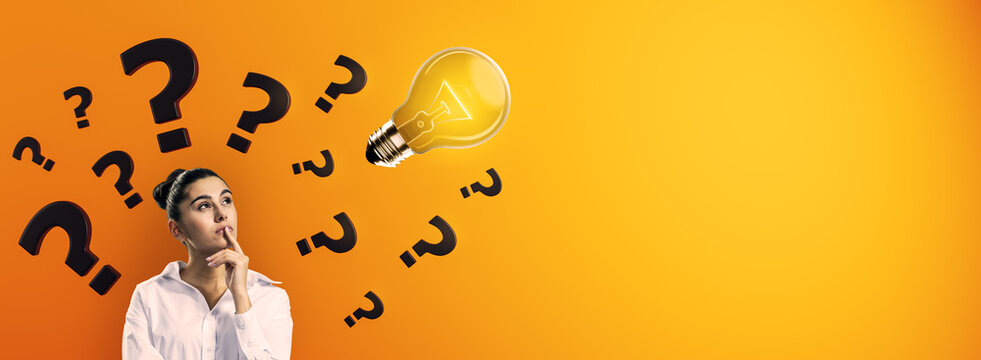 Thoughtful woman surrounded by question marks looking at glowing lightbulb on orange background symbolizing creative idea and curiosity.