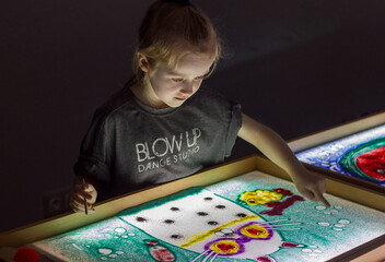 Beautiful little girl draws with sand on a light square, art therapy, sand animation, creative leisure for children, selective focus