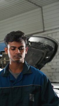 Lab technicians observe engineer demonstrating spanner use on car engine, nodding in agreement in mechanical workshop, industrial workspace features vehicles, tools, and equipment in background