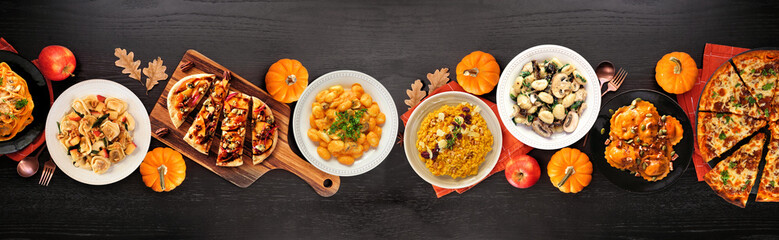 Delicious autumn meal table scene. Above view on a black wood banner background. Pumpkin and apple theme risotto, pasta, gnocchi, flat bread and pizza.