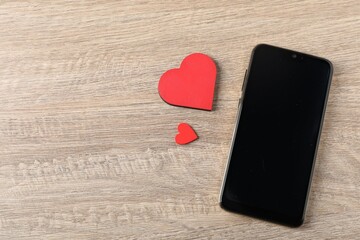 Online dating site. Smartphone and red hearts on wooden table, flat lay. Space for text