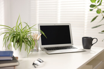 Stylish workplace with laptop, stationery and floral decor on white table in office