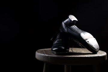 Pair of shoes for tap dance on wooden stool against black background, closeup. Space for text