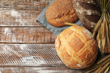 Loaves of fresh bread and wheat spikes on wooden table, flat lay. Space for text