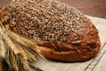 Loaf of fresh bread and wheat spikes on table, closeup