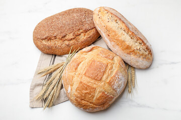 Different types of bread and wheat spikes on white marble table, flat lay