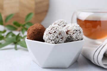 Delicious homemade candies with cocoa powder and coconut flakes in bowl on white table, closeup