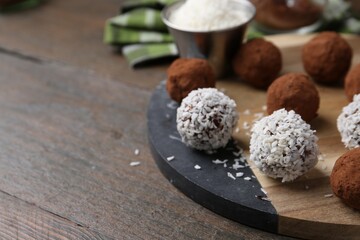 Delicious homemade candies with cocoa powder and coconut flakes on wooden table, closeup. Space for text