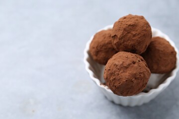 Delicious homemade candies powdered with cocoa in bowl on light table, closeup. Space for text