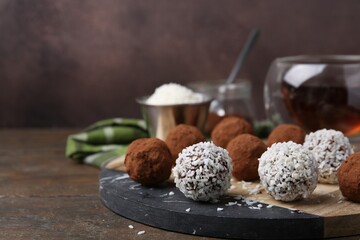 Delicious homemade candies with cocoa powder and coconut flakes on wooden table, closeup. Space for text