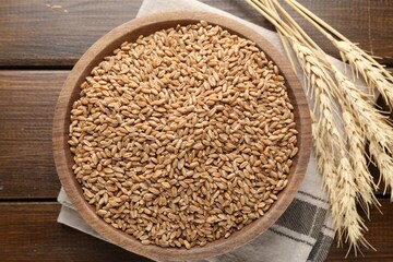 Wheat grains in bowl and spikelets on wooden table, flat lay