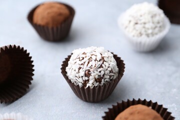 Delicious homemade candies with cocoa powder and coconut flakes on light grey table, closeup