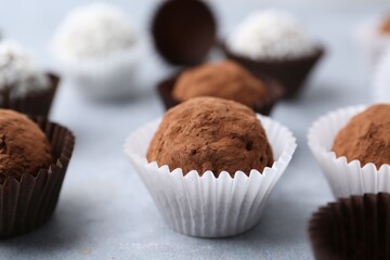 Delicious homemade candies with cocoa powder and coconut flakes on light grey table, closeup