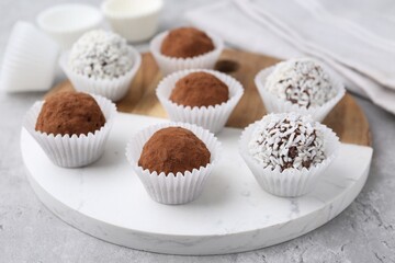Delicious homemade candies with cocoa powder and coconut flakes on light grey table, closeup