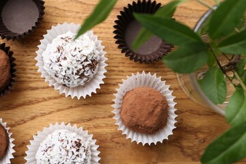 Delicious homemade candies with cocoa powder, coconut flakes and floral decor on wooden table, flat lay