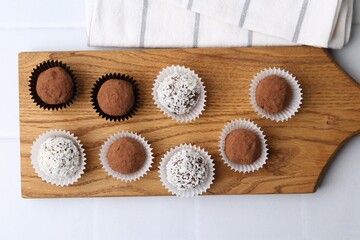 Delicious homemade candies with cocoa powder and coconut flakes on white table, top view