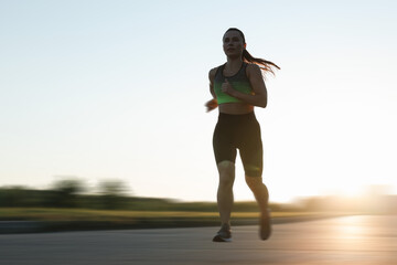 Woman in sportswear running outdoors on sunny morning, motion blur effect. Low angle view
