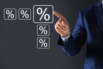 Businessman touching percent sign on virtual screen against dark grey background, closeup