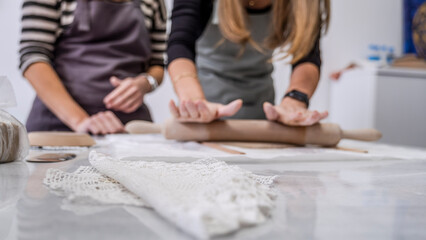 A close-up shot of a middle-aged woman artist shaping clay with a rolling pin at a table in an art studio, with an environment adorned with artistic paintings in the background