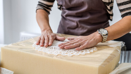In an art studio with an environment adorned with artistic paintings in the background, a beautiful middle-aged woman artist is working on a lace pattern design on a clay plate at a table