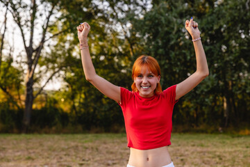 Obraz premium Young woman celebrating with raised arms in a park