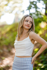 Fototapeta premium Model poses gracefully in a sunny outdoor setting surrounded by lush greenery