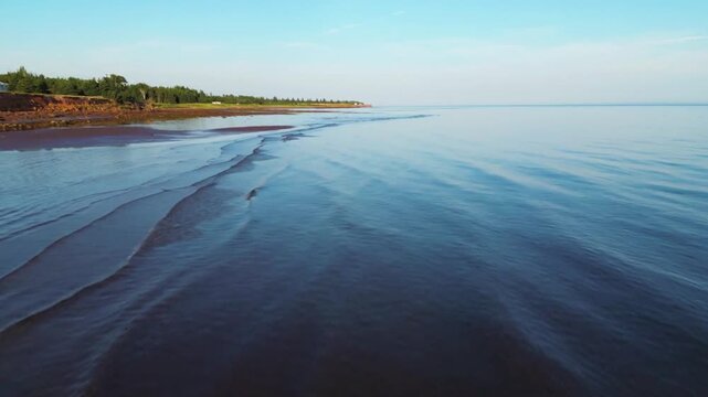 Gentle waves lap the red sand beach of prince edward island on a sunny day